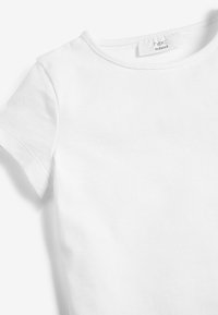 T-shirt blanc à manches courtes et col rond avec l'étiquette "next school" à l'intérieur du col, présenté sur un fond blanc.