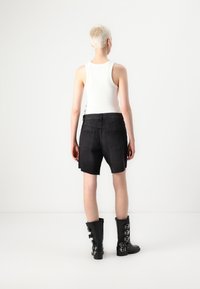 Shorts en denim noir avec un ourlet brut, associés à des bottes noires jusqu'aux genoux avec plusieurs boucles en argent. Débardeur blanc visible.