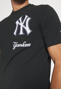 Czarny bawełniany T-shirt z dużym haftowanym logo Yankees w kolorze białym i granatowym oraz napisem "Yankees" poniżej, z krótkimi rękawami i okrągłym dekoltem.