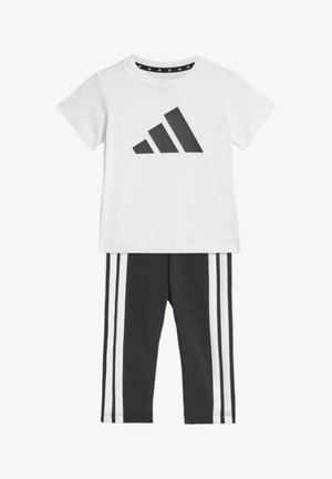 Camisa blanca de manga corta con logo negro de Adidas combinada con pantalones negros con tres rayas verticales blancas en cada pierna.