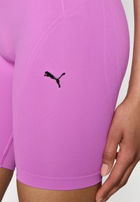Shorts de sport ajustés violets en tissu extensible, ornés d'un petit logo noir Puma sur le côté et d'une finition lisse et texturée.