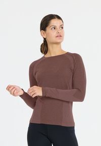 Pitkähihaista ruskeaa urheilu paitaa, jossa on värilliset sivupaneelit ja sileä vartalo. Mukana ribbed-yksityiskohdat hihoissa ja olkasaumoissa.
