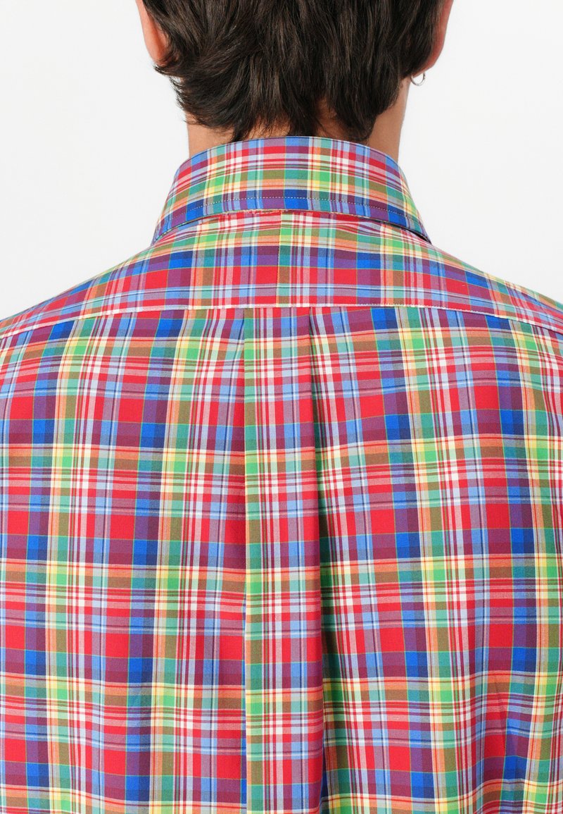 Koszula w wielokolorową kratę z czerwonymi, niebieskimi, zielonymi i żółtymi wzorami. Lekka tkanina, klasyczny kołnierzyk i fason z plisowanym tyłem.
