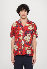 Punainen lyhythihainen paita, jossa on kukkakuosi, jossa on suuria valkoisia ja keltaisia kukkia, vihreitä lehtiä ja mustia yksityiskohtia; napitus.