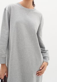 Graues Sweatshirtkleid mit langen Ärmeln, Rundhalsausschnitt und gerippten Bündchen. Weicher Stoff mit lockerer Passform und seitlichen Taschen.