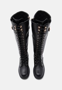 Czarne skórzane kozaki do kolan z sznurówką z przodu, metalowymi oczkami i pikowanymi detalami u góry. Gładka powierzchnia.