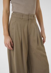 High-waisted, pleated trousers made of lightweight, tan fabric. Features side pockets and a smooth texture.