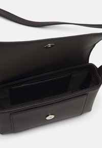 Tummanruskea nahkainen olkalaukku, jonka läppä on auki, paljastaen sisäpinnan kangasta ja etutaskun magneettisella sulkimella.