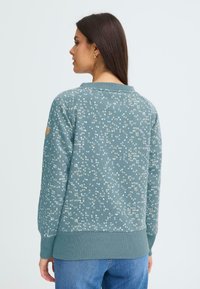 Felpa verde con motivi circolari bianchi e beige, polsini e orlo a costine. Tessuto morbido, design a girocollo, etichetta del marchio visibile sulla manica.