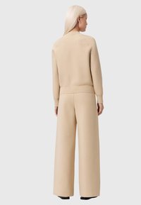 Conjunto de suéter beige y pantalones de pierna ancha, confeccionado en tela suave, con puños y cinturilla acanalados, textura lisa y corte relajado.