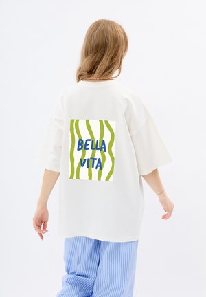 T-shirt élégant surdimensionné blanc avec un graphisme à rayures vertes et blanches au dos, présentant le texte "BELLA VITA" en bleu.