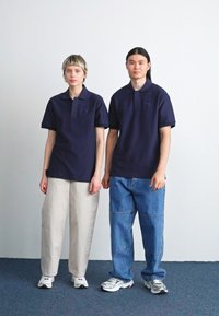 Námornícky modré polo tričká s krátkymi rukávmi a textúrovaným vzorom, v kombinácii so svetlými nohavicami. Biele tenisky dopĺňajú outfity.