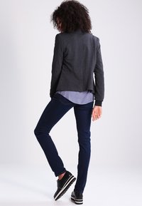 Charcoal blazer with a fitted design, featuring a rounded hem and back vent, layered over a light blue shirt, paired with dark jeans and black sneakers.