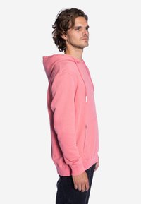 Roze hoodie gemaakt van zachte stof, met een voorzak, geribde manchetten en een klassieke pasvorm. Geen zichtbare patronen of hardware.