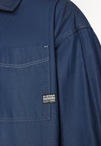 Marineblå denimskjorte med brystlomme, kontrasterende syninger og G-Star logo-tag; har en klassisk krave og afslappet pasform.
