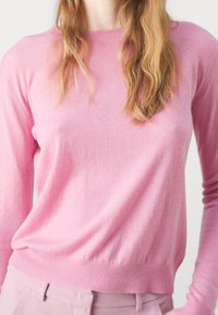Różowy sweter z kaszmiru z długimi rękawami, okrągłym dekoltem i ściągaczem na dole. Miękka tekstura i lekki materiał. Minimalistyczny design.
