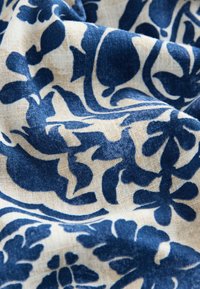 Puuvillakangas, jossa sininen kukkakuvio beigen taustan päällä. Tekstuuri on pehmeä, ja koko pinnalla on näkyvissä kudontakuvioita.