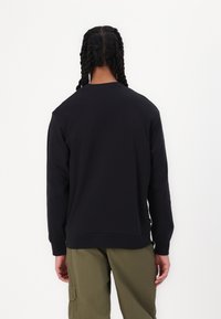 Zwarte sweatshirt met lange mouwen, ronde hals en geribbelde manchetten. Gladde textuur, eenvoudige ontwerpeisen en valt onder de taille. Gepaard met groene broeken.