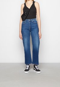 Jeans in denim blu a vita alta con gamba dritta, leggermente sbiaditi con design a cinque tasche, abbinati a sneakers nere in tela.