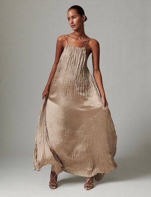 Bezs színű, fodros textúrájú szatén maxi ruha, vékony pántokkal és légies sziluettel, vékony pántos magassarkúkkal párosítva.