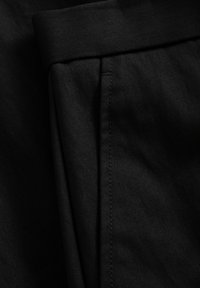 Közeli kép fekete szövetből, varrott varrással és hajtott szegéllyel, amely megmutatja a ruha textúráját és a részletes szabást.