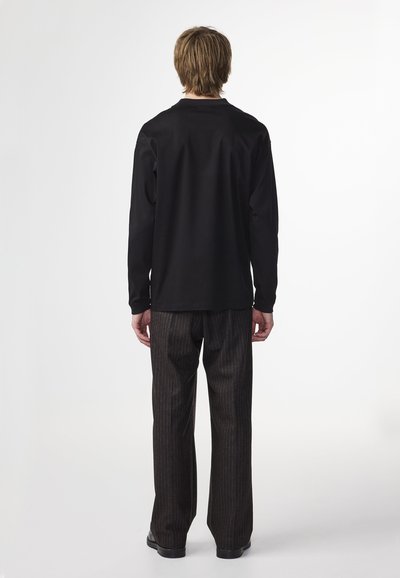 Black long-sleeve shirt paired with dark striped pants. Soft texture, relaxed fit, and minimalistic design, viewed from the back.