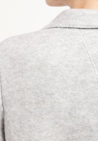 Szary kołnierz filcowej kurtki o miękkiej fakturze, z widocznymi przeszyciami i czystym, minimalistycznym designem. Widok z tyłu ukazuje szwy.