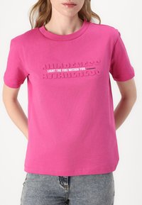 Rosa crewneck t-skjorte med hevet tekst som lyder "BEVISSTHET TENN ILLEN INNI DEG." Korte ermer, glatt bomullstoff.