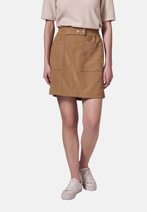Jupe kaki de forme évasée, avec une taille élastique, deux poches avant et des clous argentés le long des poches. Assortie avec des baskets blanches.