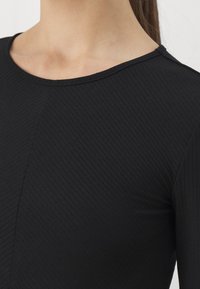Top nero a coste con scollatura rotonda. Presenta una superficie testurizzata e un design aderente. Il tessuto segue da vicino la forma del corpo.