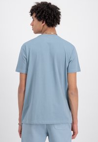 T-shirt iz bombaža v nebeško modri barvi z kratkimi rokavi, sproščenega kroja, minimalni šivi. Gladka tekstura in okrogla vrata.