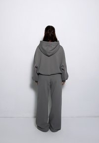 Szara, przero�śnięta bluza z kapturem i różowymi akcentami w szwie, w zestawie z dopasowanymi spodniami o szerokich nogawkach, wykonanymi z miękkiego materiału. Widok z tyłu.