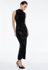 Svart sammetskvällkl�änning med en figurnära silhuett, asymmetrisk halsringning och rynkdetaljer. Bärs med svarta högklackade skor.