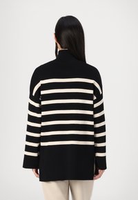 Suéter de punto a rayas negras y crema con cuello alto, corte holgado y mangas largas. Presenta rayas horizontales en contraste en la parte trasera.