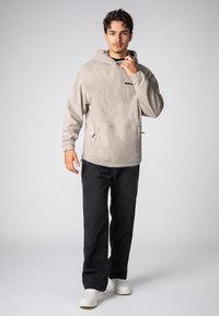 Hellgrauer Fleecepullover mit Kapuze und vorderer Tasche, dazu schwarze Jeans und weiße Turnschuhe. Schlichtes und bequemes Design.