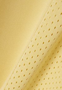 Primer plano de tela amarilla que muestra dos texturas textiles: tejido sólido y tejido perforado con pequeños agujeros.