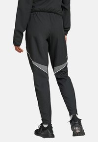 Pantalons de sport noirs avec une finition texturée, dotés d'accents latéraux réfléchissants et d'une coupe cintrée, associés à des chaussures de course noires.