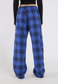 Blauwe geruite wijde broek met zwarte accenten, elastische tailleband en zachte stof. Heeft een subtiel ruitpatroon door het hele ontwerp.