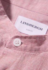 Camicia di lino rosa chiaro con un design slim-fit, dotata di un bottone bianco e un'etichetta con la scritta "LINDBERGH SLIM FIT" vicino al colletto.