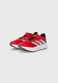 Red athletic shoes with a mesh upper, black accents, silver stripes, and a white midsole. Includes black laces and reinforced toe area.
