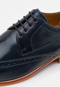 Scarpa da uomo in pelle navy con finitura liscia, dotata di lacci rotondi, dettagli perforati lungo i lati e suola marrone a contrasto.