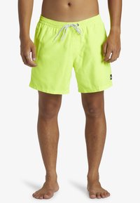 Bañador amarillo neón hecho de tela ligera, con una cinturilla elástica y cordón ajustable, y una pequeña etiqueta negra con el logo en el lateral.