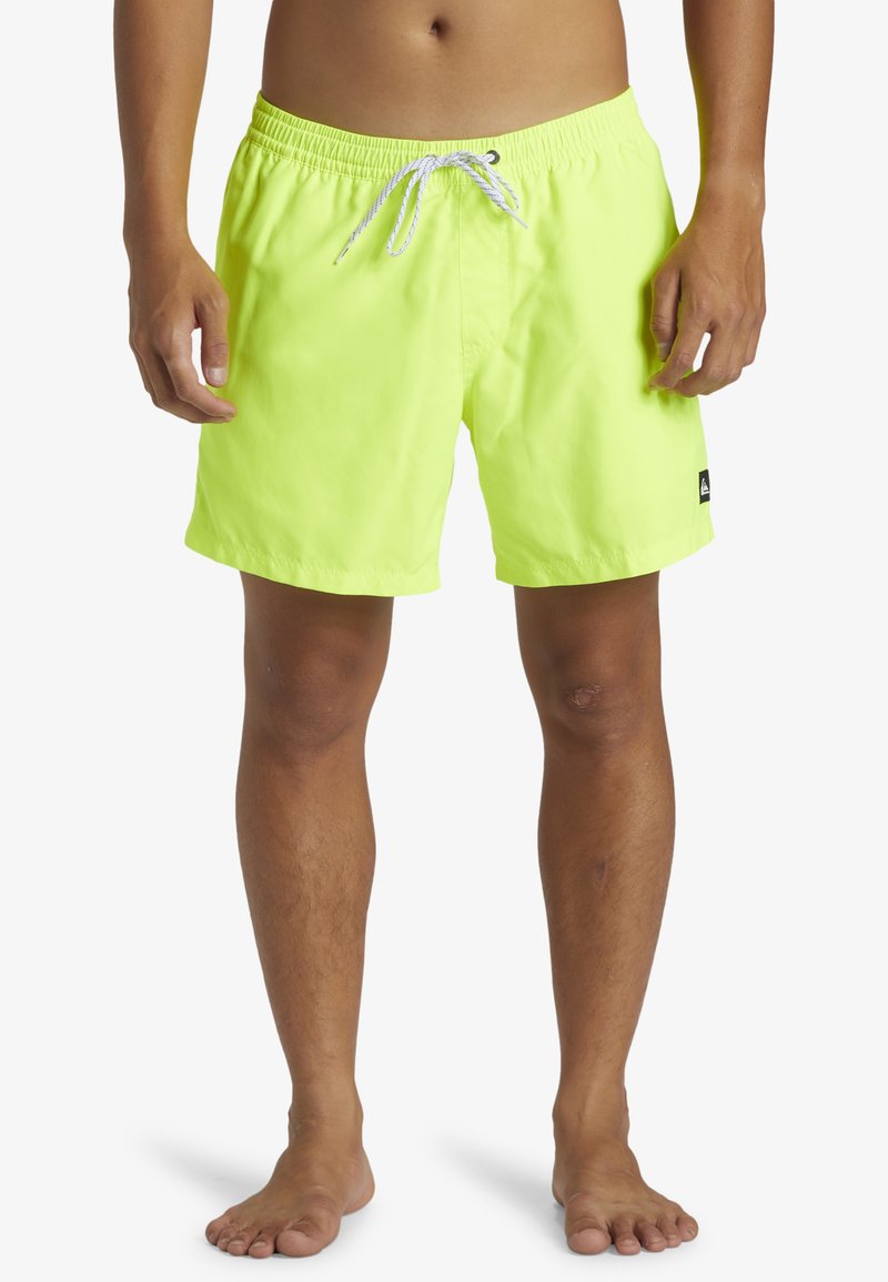 Bañador amarillo neón hecho de tela ligera, con una cinturilla elástica y cordón ajustable, y una pequeña etiqueta negra con el logo en el lateral.