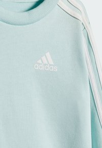 Sudadera azul claro con un tejido texturizado, que presenta el logo de adidas en blanco y acentos a rayas blancas en los hombros.