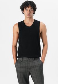 Schwarzes ärmelloses Strickoberteil mit einem runden Halsausschnitt, kombiniert mit grauen karierten Hosen mit Knopfverschluss und Taschen.