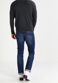 Sweater gris, jeans azules con dobladillos, calcetines blancos con acentos rojos. Detalles notables: bolsillos traseros, forma ajustada, diseño casual.