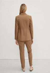 Bruin maatpak met een aansluitend colbert en bijpassende taps toelopende broek, gemaakt van gladde stof, met strakke lijnen en zichtbare stikdetails.