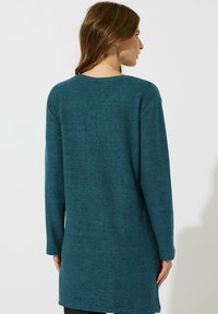 Abito lungo teal a maniche lunghe con una vestibilità comoda, realizzato in tessuto a maglia testurizzato. Presenta un collo rotondo e arriva a metà coscia sul retro.