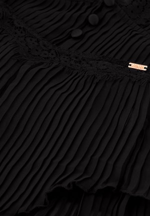 Sort plisseret stof med blonder, to runde knapper og et lille metallskilt. Tekstur overflade med et flydende design og flæset kant.