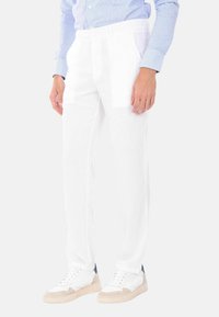 Pantaloni di lino bianchi con un design a gamba dritta, dotati di tasche laterali e una sottile texture, abbinati a sneakers bianche e beige.